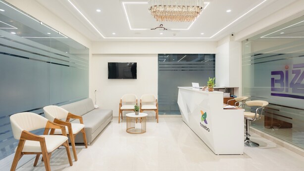 A modern reception area with a white reception desk, a sofa, and two wooden chairs. - Treebo Premium Bizz (Ahmedabad)