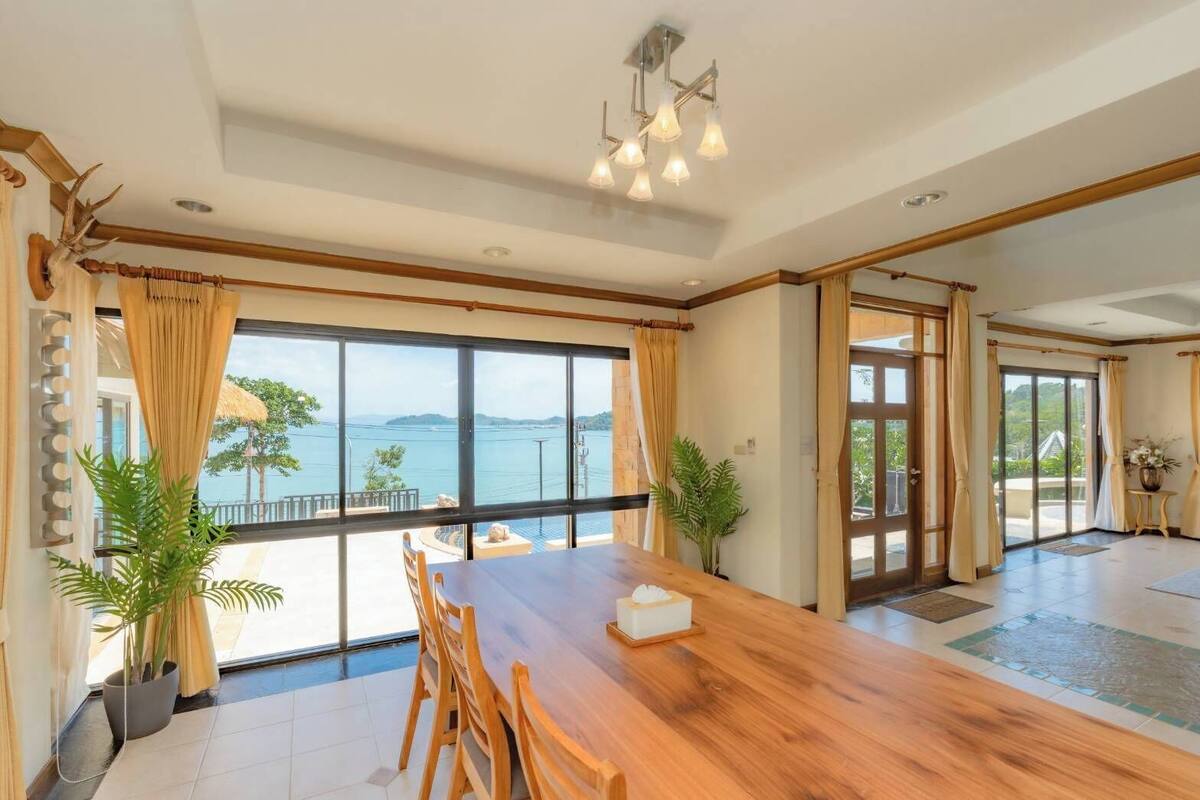 Une pièce spacieuse avec une grande table en bois, de nombreuses fenêtres et une vue sur la mer.