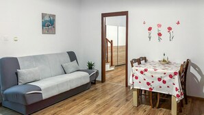 Ein modernes Wohnzimmer mit einem grauen Sofa, einem Esstisch mit rotem Blumentuch und Holzboden.