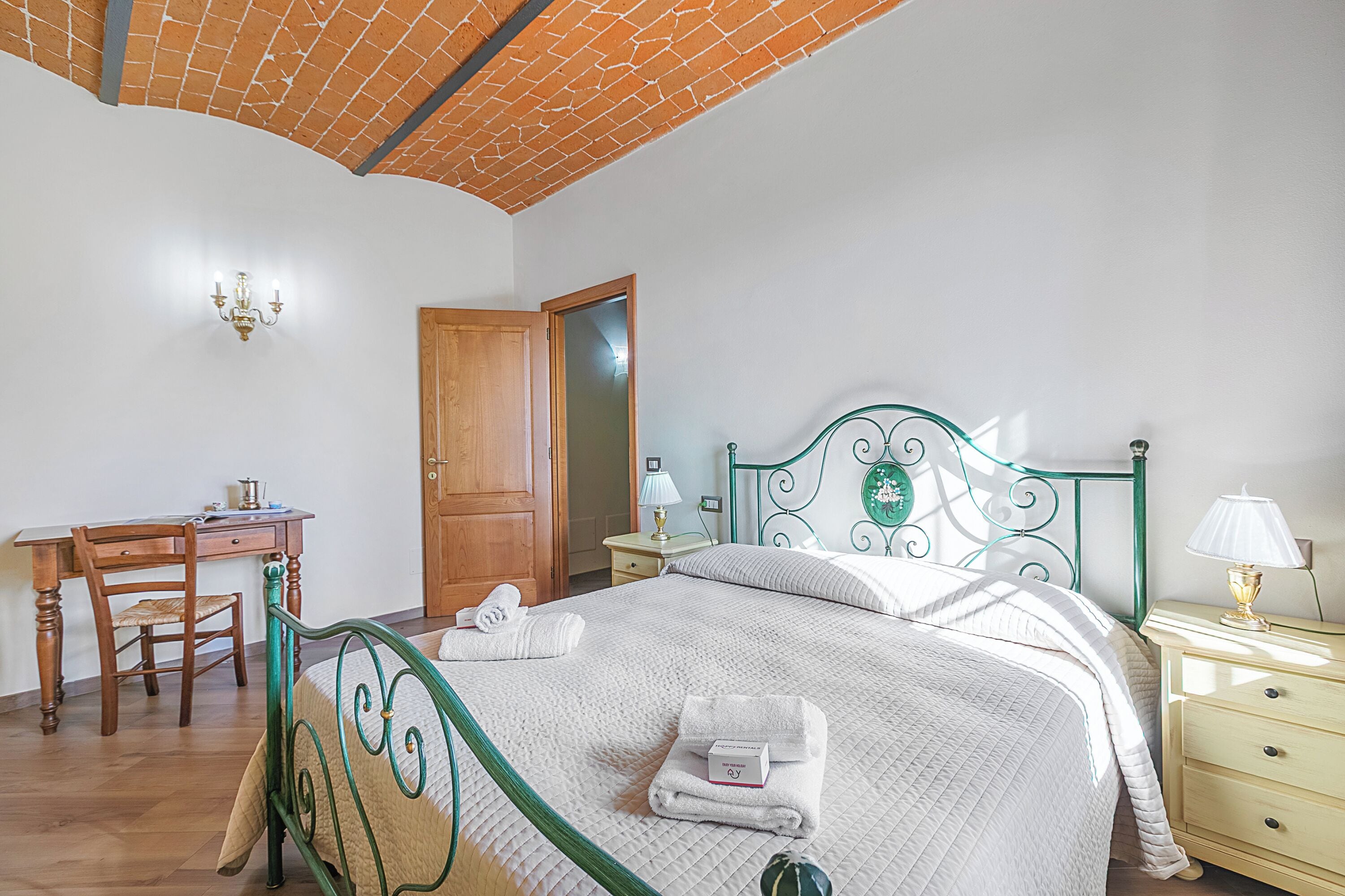 Een slaapkamer met een bed, een bureau, een stoel, een nachtkastje en een lamp.