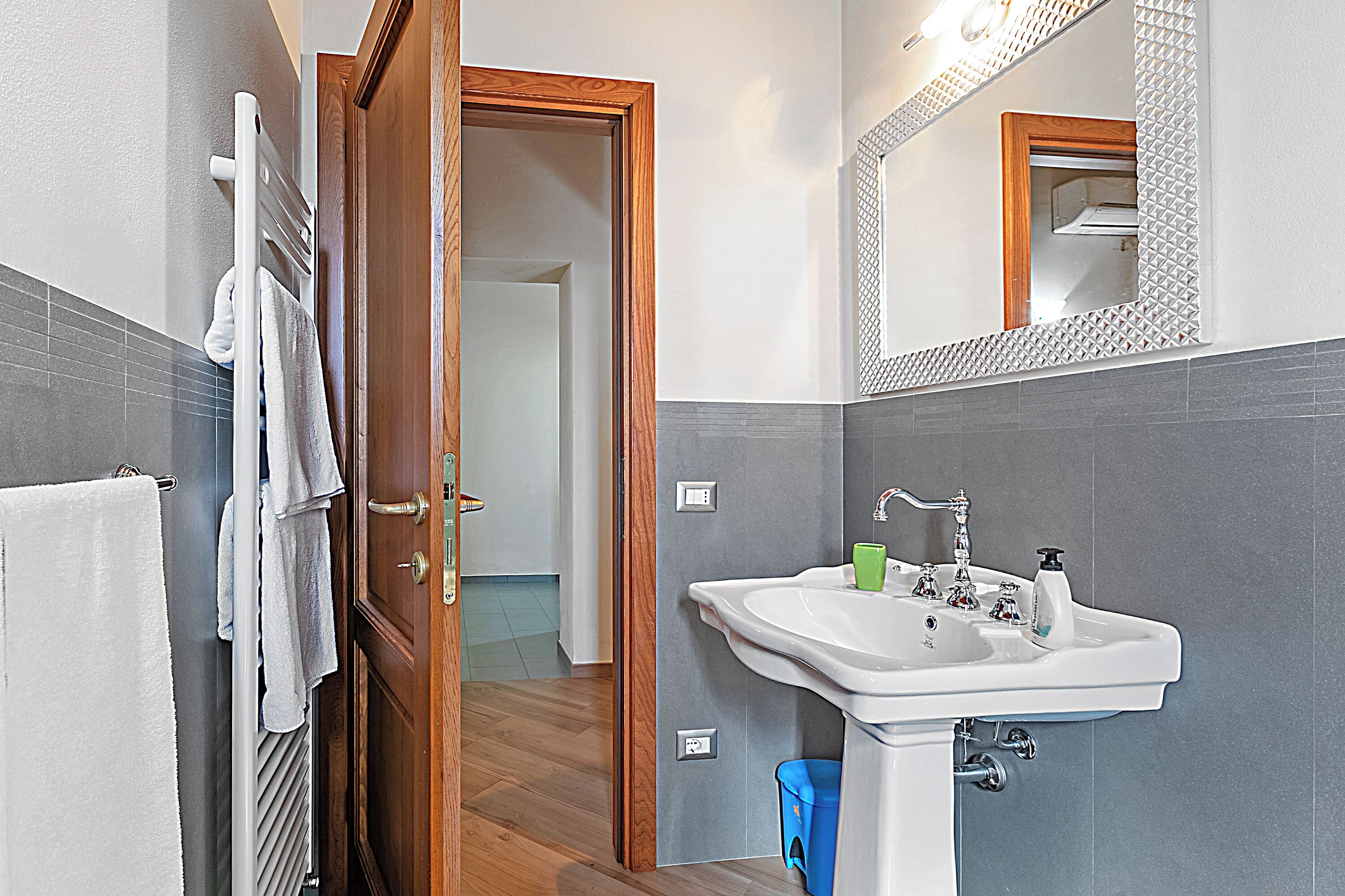 Une salle de bain avec un lavabo blanc, un miroir et une porte en bois.
