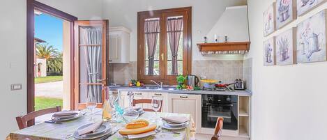 Un coin repas avec une table dressée pour quatre personnes, une cuisine équipée d’appareils modernes et une vue sur l’extérieur.