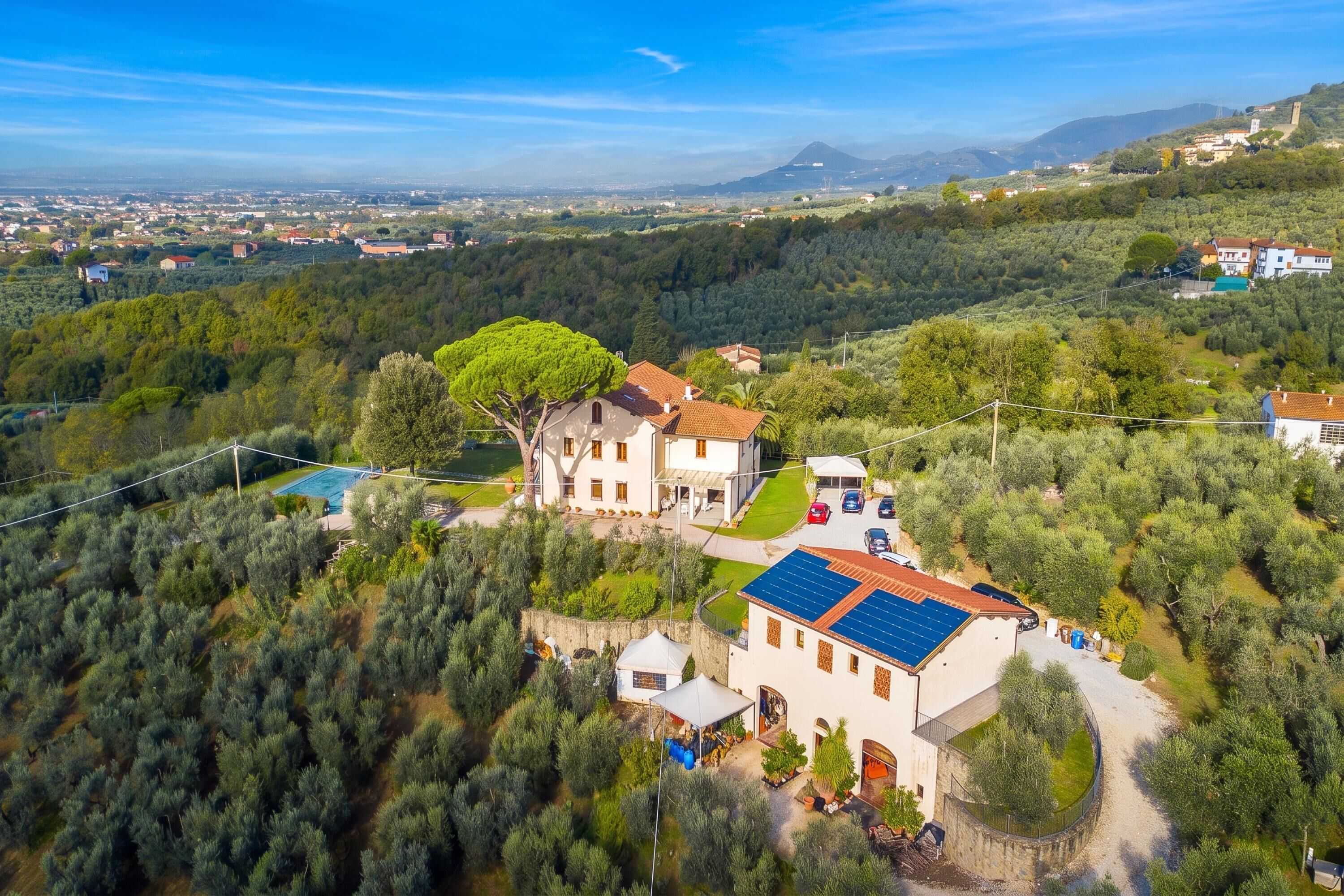 Une grande villa avec piscine, entourée d’une forêt dense, et offrant une vue sur la ville, qui se trouve au loin.
