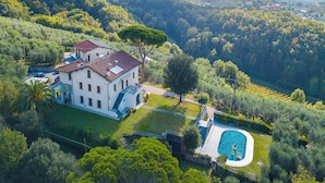 Una villa grande y blanca con techo rojo, rodeada de exuberante vegetación y una piscina.