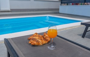A poolside table with croissants and a glass of orange juice.