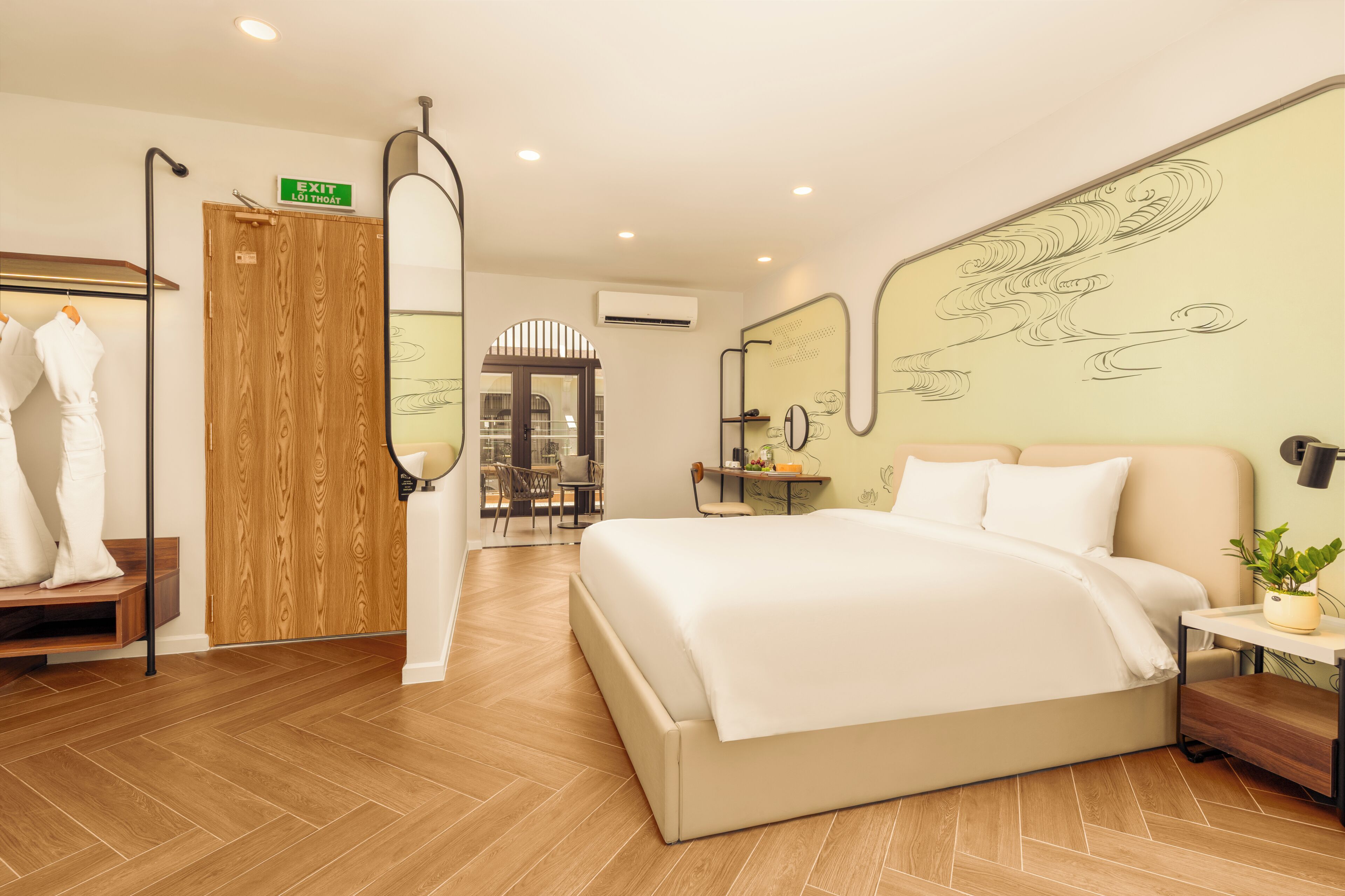 Ein Hotelzimmer mit Bett, Kleiderschrank, Spiegel, Schreibtisch mit Pflanze und Blick auf die Stadt durch das Fenster.