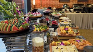 A buffet with various food items and a large window with a view of palm trees. - Lumiere Boutique Vy Da (Hue)