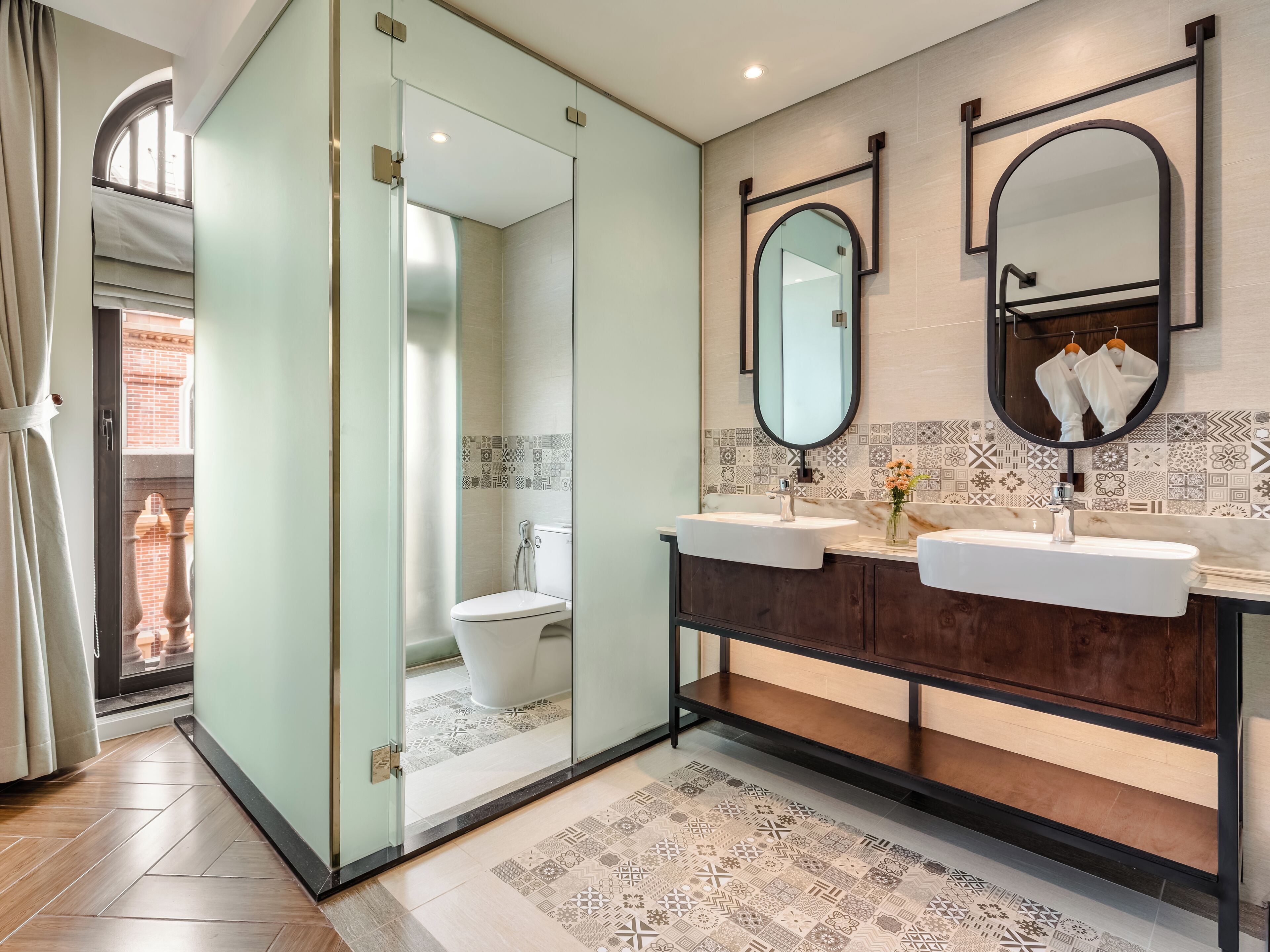 A modern bathroom with a glass partition, two sinks, a large mirror, and patterned tiles.