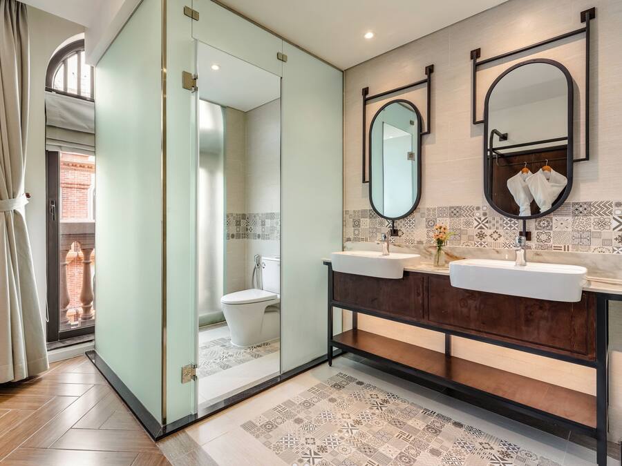 A modern bathroom with a glass partition, two sinks, a large mirror, and patterned tiles.