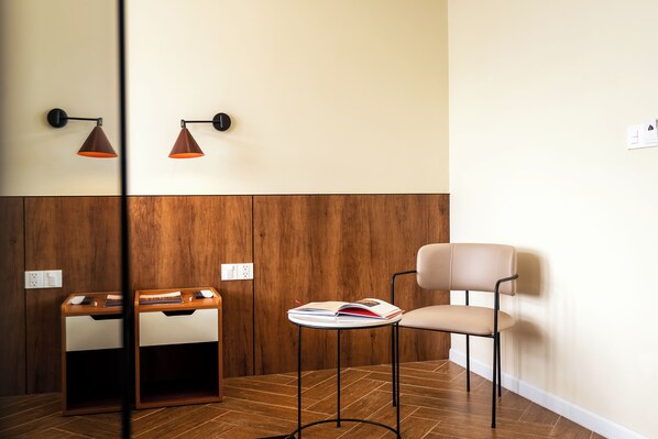 A room with a wooden wall panel, a wooden side table with a book, a chair, and two wall-mounted lamps. - Lumiere Boutique Vy Da (Hue)