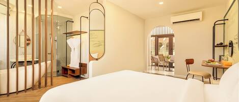 A hotel room with a large bed, a bathroom with a bathtub, a shower, and a seating area with a table and chairs.