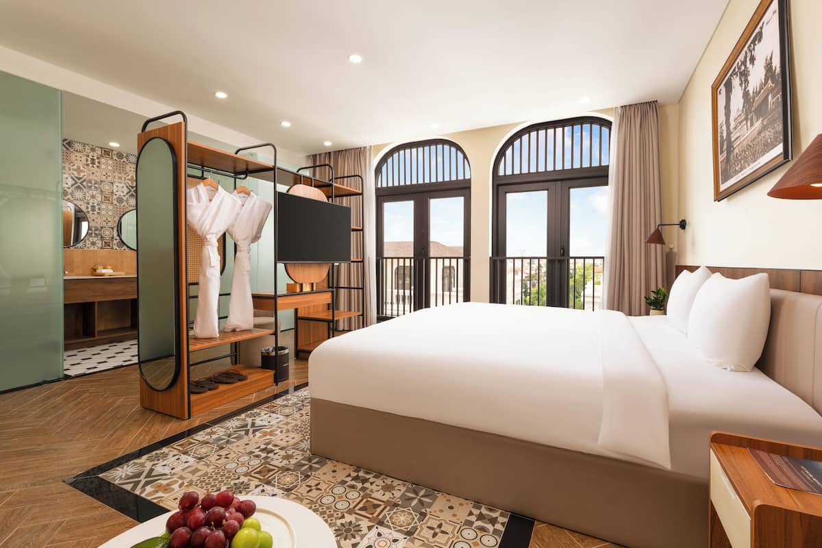 Una camera d'albergo con un letto grande, una toeletta con specchio, una TV e un balcone con vista.