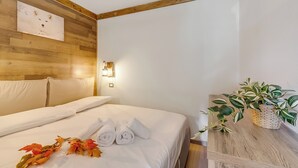 Habitación de hotel con cabecera de madera, cama con ropa de cama blanca, mesita de noche con una planta y una lámpara fijada a la pared.
