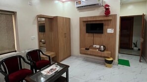 A living room with a sofa, two armchairs, a coffee table, a TV mounted on a wooden wall, and an air conditioning unit. - JSB PALACE (Varanasi)