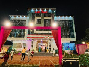 A building with a sign reading "J.S.B. ALAC" at the top, featuring a large entrance with a red archway and multiple windows adorned with string lights. - JSB PALACE (Varanasi)