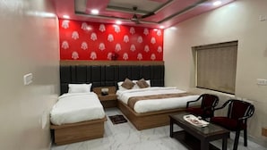 A hotel room with two beds, a sofa, a small table, and a ceiling fan. - JSB PALACE (Varanasi)