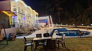 A hotel with a swimming pool, outdoor seating, and a well-lit entrance. - Haveli Resort Shivpuri (Rishikesh)