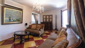 Een woonkamer met een zwart-witte vloer, een bank, een tafel, een kroonluchter en een schilderij aan de muur.