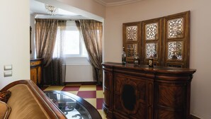 Een kamer met een geruit vloerkleed, een houten kast met decoratieve panelen, een bank en een raam met gordijnen.