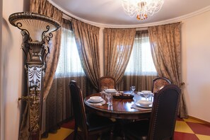 A dining room with a round table set for four, surrounded by chairs. There is a decorative metal stand on the left and a chandelier above. - Villa Ioannis (Mandra Eidyllia)