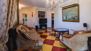 Een woonkamer met een zwart-wit schakeerd patroon op de vloer, een kroonluchter, een televisie en een schilderij aan de muur.