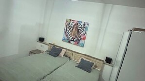 A bedroom with two beds, a wall-mounted painting of a tiger, a white ceiling fan, and a white refrigerator. - Emsquartier 2 (Emsdetten)