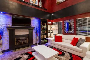 A modern living room with a fireplace, white sofa, and red cushions. - Coratel Inn and Suites By Jasper Wichita North -Standard 2 Queen Bed NS (Wichita)