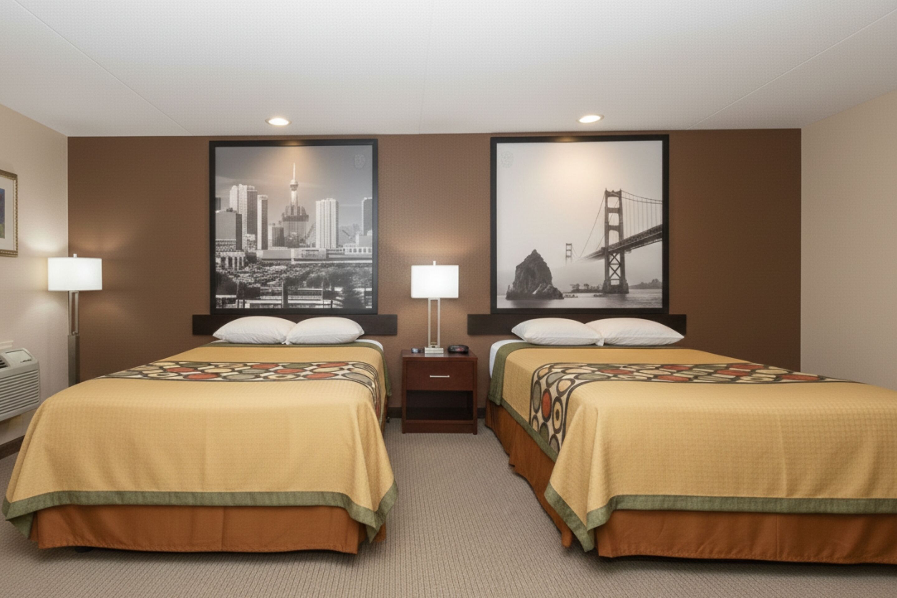 A hotel room with two beds, a nightstand, a lamp, and two large framed pictures on the wall.