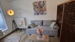A modern living room with a grey sofa, a wooden coffee table, a floor lamp, and a painting of a tiger on the wall. - Emsquartier 1 (Emsdetten)