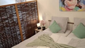 A neatly made bed with a green blanket and pillows, a wooden headboard, and a painting on the wall. - Emsquartier 1 (Emsdetten)