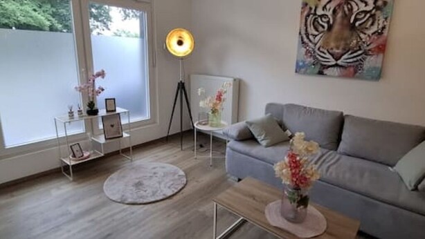 A modern living room with a grey sofa, a round coffee table, and a painting of a tiger on the wall. - Emsquartier 1 (Emsdetten)