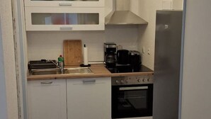 A compact kitchen with white cabinets, a stainless steel refrigerator, a coffee maker, and a toaster. - Emsquartier 1 (Emsdetten)