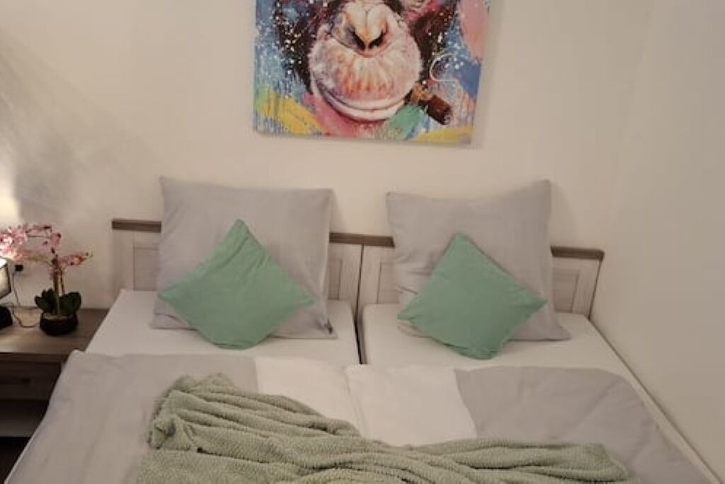 A bed with two pillows, a blanket, and a painting on the wall.