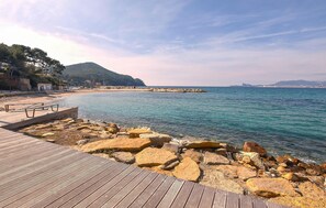 Une promenade en bord de mer avec une terrasse en bois, une côte rocheuse et une vue sur la mer et le paysage urbain lointain.