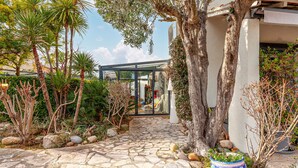 A stone-paved pathway leading to a modern glass structure, surrounded by various plants and trees. - Awesome home in Six-Fours-les-Plages (Six-Fours-les-Plages)
