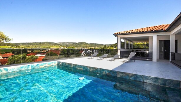 A swimming pool with clear blue water, a covered patio with lounge chairs, and a view of the countryside. - Villa avec piscine privée (Portel des Corbières)