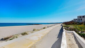 A coastal road with a beach on one side and a row of modern buildings on the other. - Villa avec piscine privée (Portel des Corbières)
