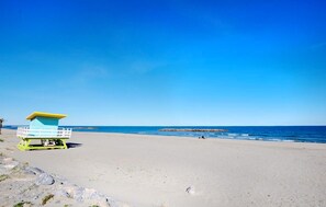 Uma praia com uma torre salva-vidas, céu azul límpido e mar calmo.