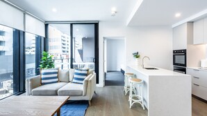 A modern apartment with a living area featuring a sofa, a coffee table, and a view of the city. - Preston Rooftop Oasis - Pool, Views & City Access (Preston)