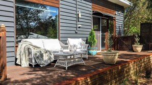 Un espacio de estar al aire libre cubierto con un sofá y una mesa, plantas en macetas y una terraza de madera.