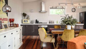 Una cocina moderna con armarios oscuros, una encimera blanca y un comedor con mesa de madera y sillas amarillas.