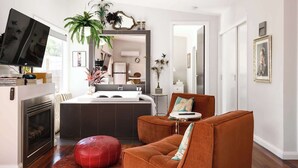 Una sala de estar moderna con chimenea, un reposapiés rojo, un sofá marrón y una cocina al fondo.