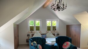 A spacious attic bedroom with a sloped ceiling, two windows with shutters, a chandelier, and a bed with pillows. - Vacation apartment Kunterbunt (Bad Reichenhall)
