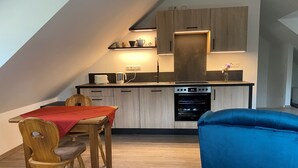 A modern kitchen with wooden cabinets, a dining table with chairs, and a blue sofa. - Vacation apartment Kunterbunt (Bad Reichenhall)