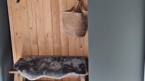 Een houten bank met een bont plaid, een geweven mand en metalen haken aan een muur.