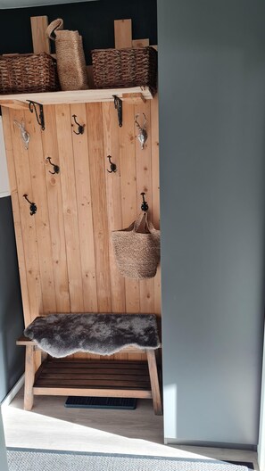 Eine Holzbank mit einem Fellüberwurf, einem gewebten Korb und Wandhaken aus Metall.