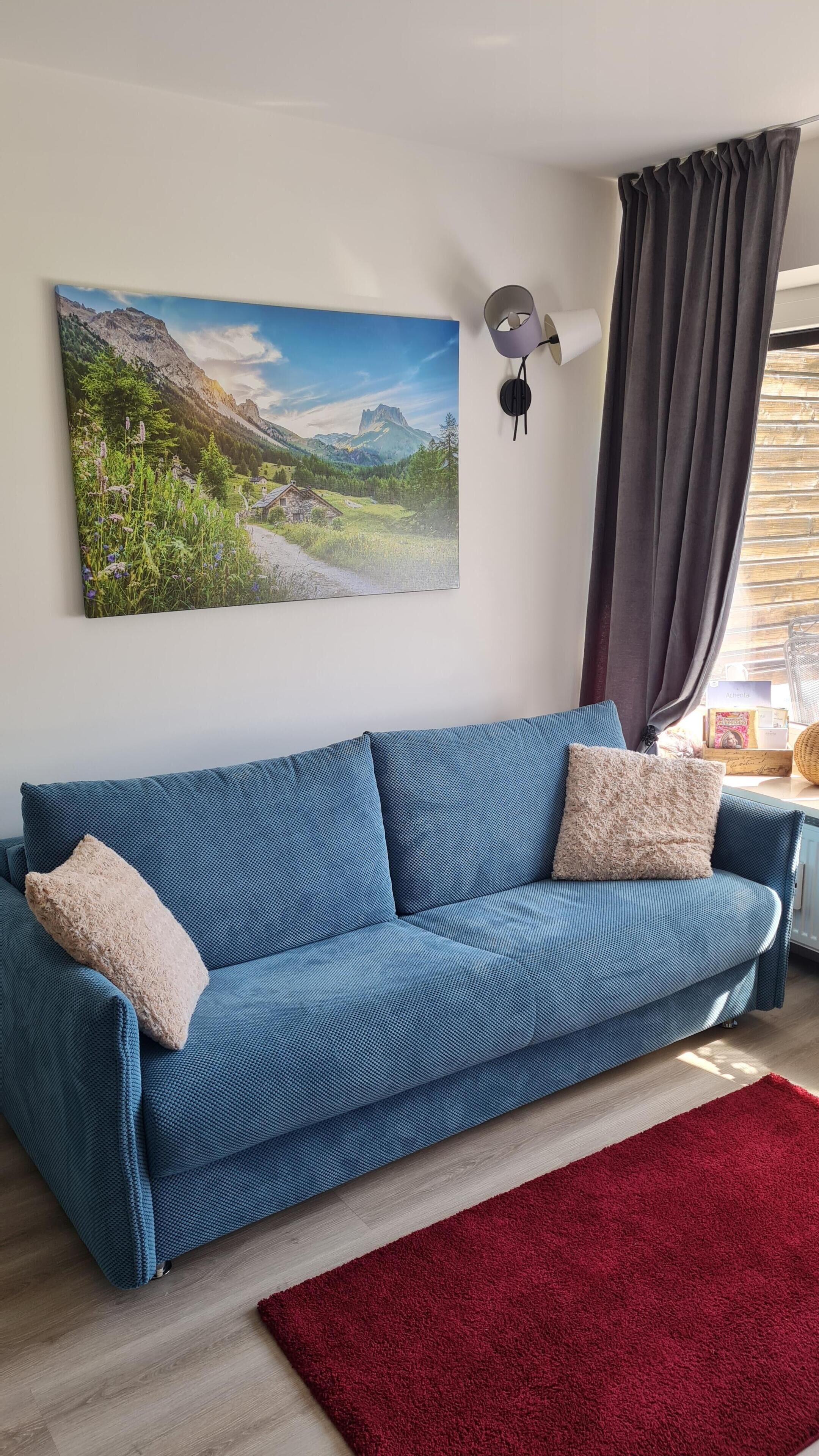 Ein blaues Sofa mit einem roten Teppich, einer Wandleuchte und einem Landschaftsbild.