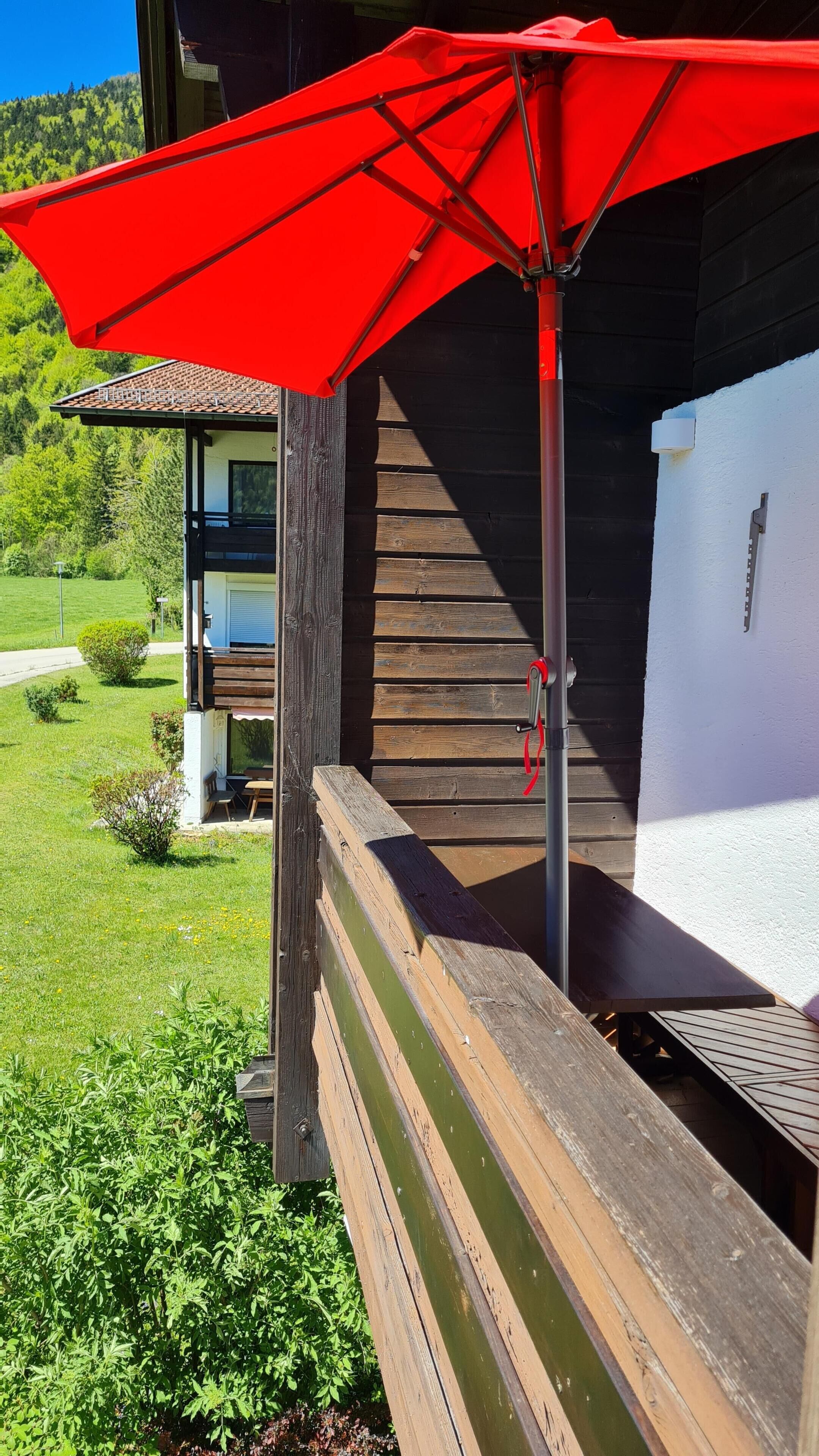 Una terraza de madera con un paraguas rojo, una escalera y un edificio blanco con una ventana.