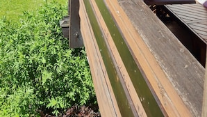 Een houten terras met een rode parasol, een trap en een wit gebouw met een raam.