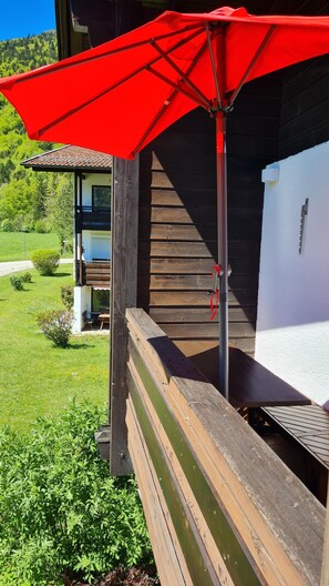 Eine Holzterrasse mit einem roten Sonnenschirm, einer Treppe und einem weißen Gebäude mit einem Fenster.